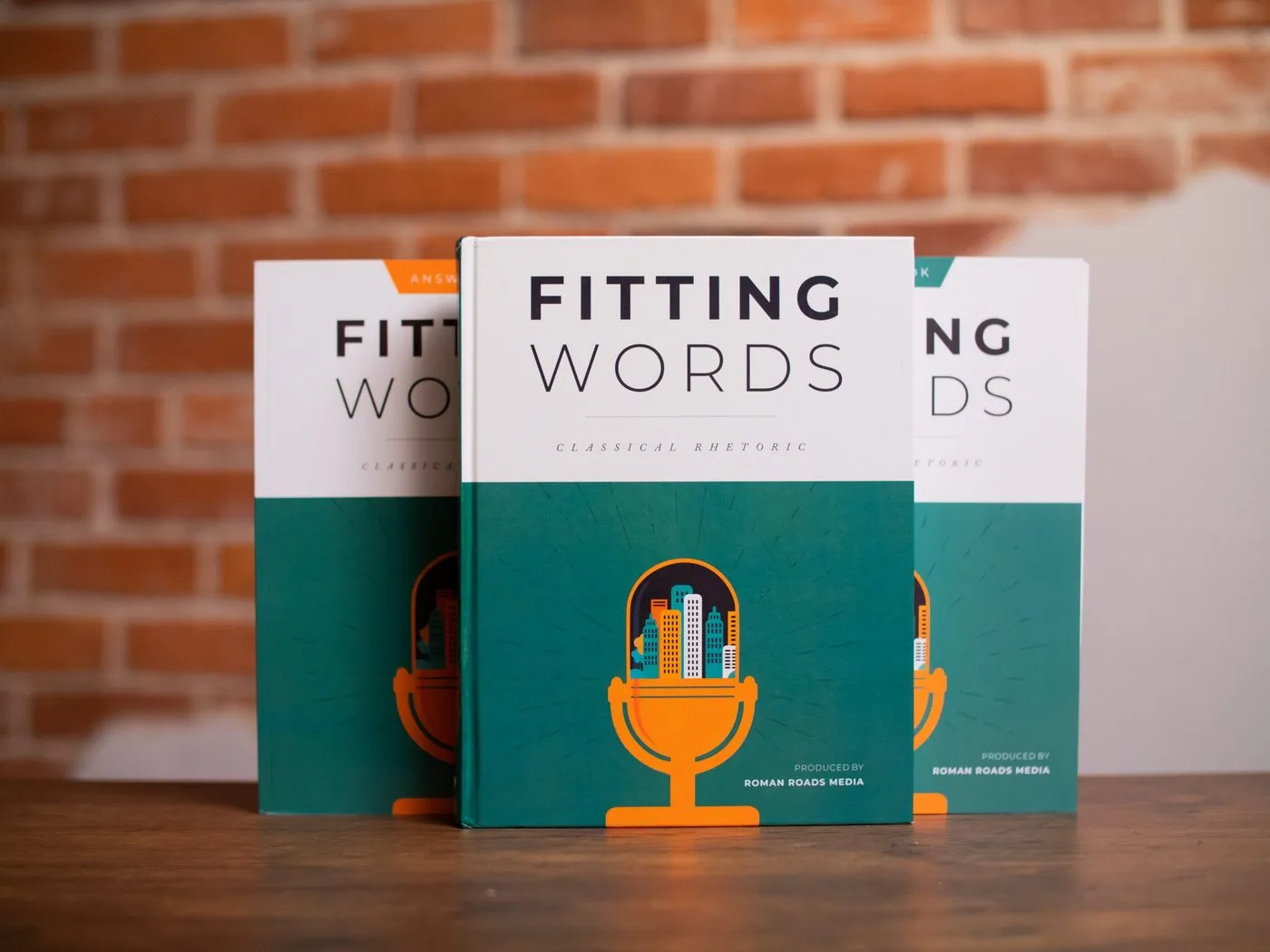 The Fitting Words textbook, workbook and answer key on a table, with an orange microphone